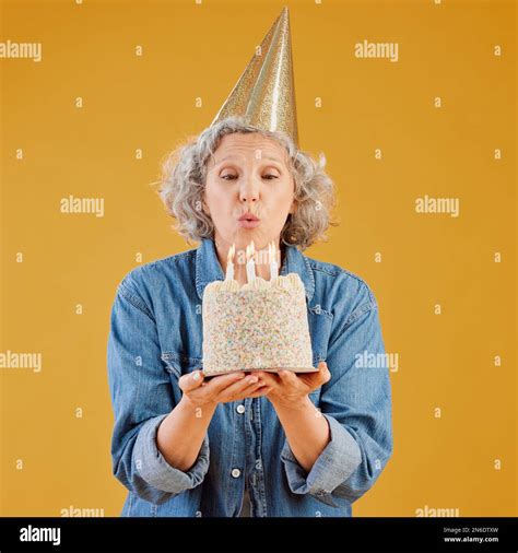 One Happy Mature Caucasian Woman Blowing Out Candles On A Cake She Is