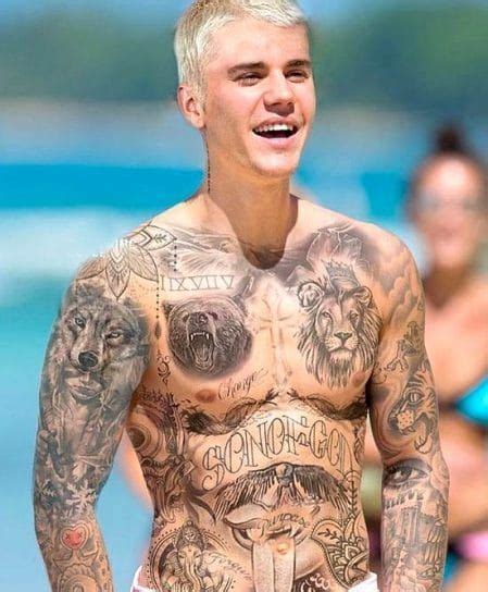 A Man With Lots Of Tattoos On His Body And Chest Standing In Front Of The Ocean