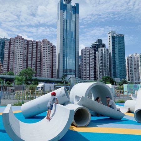 Two People Climbing Up And Down A Slide In A Playground With Buildings