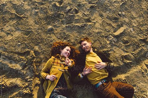 Young Couple Looking To Each Other Laying On The Sand By Stocksy