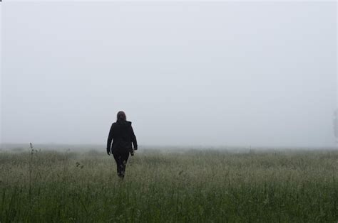 Vista Trasera De Una Mujer Caminando Por Un Campo De Hierba En Un Clima