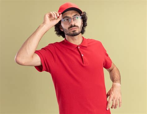 Entregador jovem caucasiano confuso uniforme vermelho e boné de