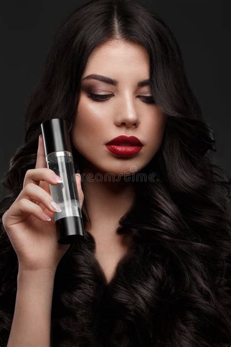 Beautiful Brunette Model Curls Classic Makeup And Red Lips With A Bottle Of Hair Products The