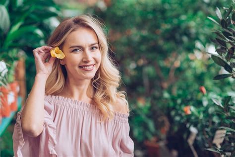 Souriant Portrait De Jeune Femme Blonde Tenant Une Fleur Jaune Dans Son Oreille Photo Gratuite