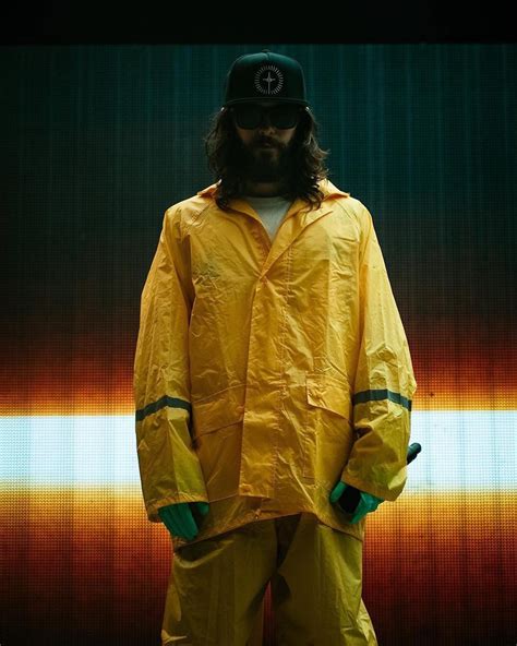 A Man With Long Hair Wearing A Yellow Rain Suit And Black Hat Standing