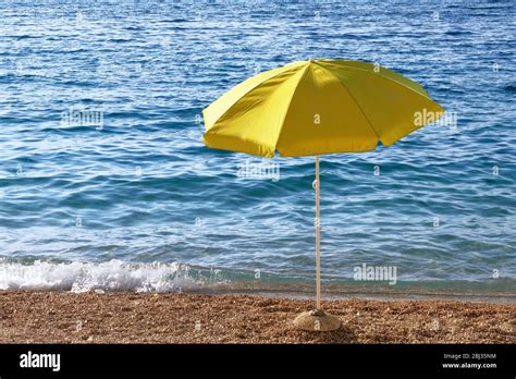 Yellow beach umbrella on summer coast. Sea beach with sun umbrella is waiting for tourists on ...