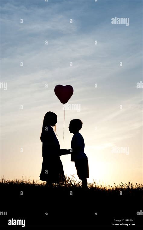 Silhouette Of A Young Girl And Boy Holding Hands With A Heart Shape