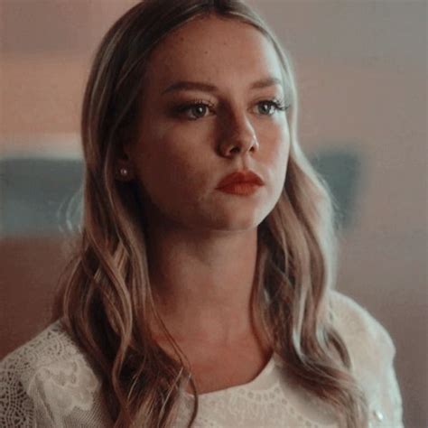 A Woman With Long Blonde Hair Wearing A White Shirt And Earrings