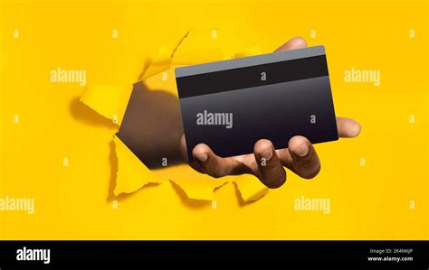 Black Male Hand Holding Bank Credit Card In Torn Hole Of Yellow