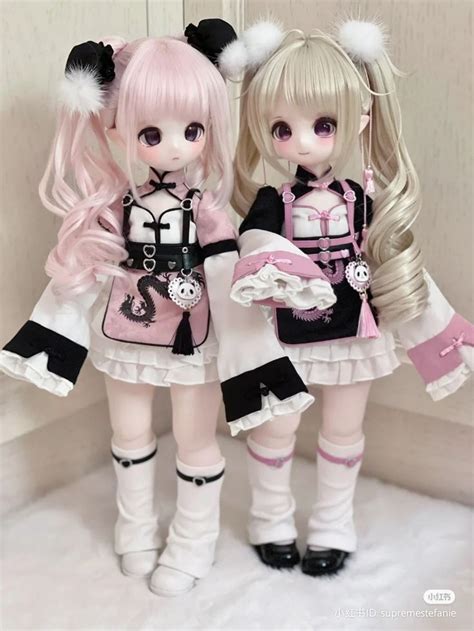 Two Dolls Standing Next To Each Other In Front Of A White Wall With