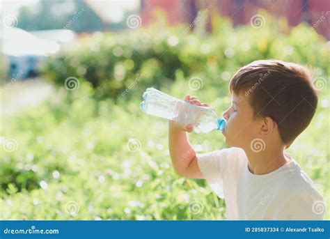 Cute Boy Sitting On The Grass Drinks Water From A Bottle In The Summer