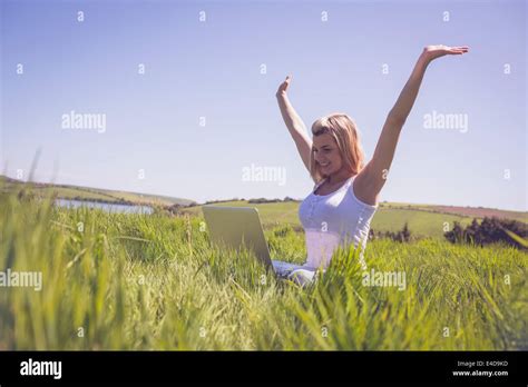 Pretty Blonde Sitting On Grass Using Her Laptop And Cheering Stock