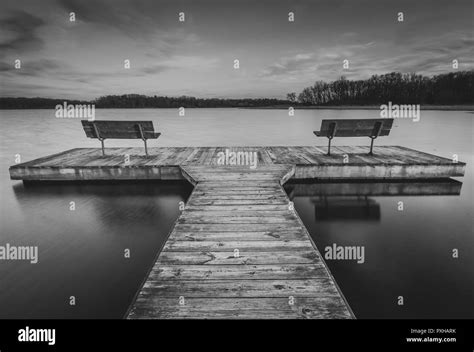 A Lonely Pier In Black And White With Two Benches Sitting On A Calm