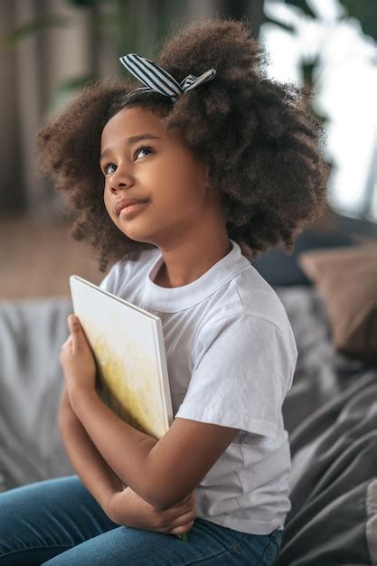 Une Fille Aux Cheveux Bouclés Assise Sur Le Lit Et Ayant L air Rêveuse