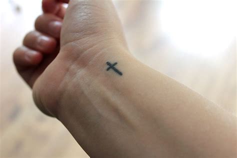 A Person With A Small Cross Tattoo On Their Arm