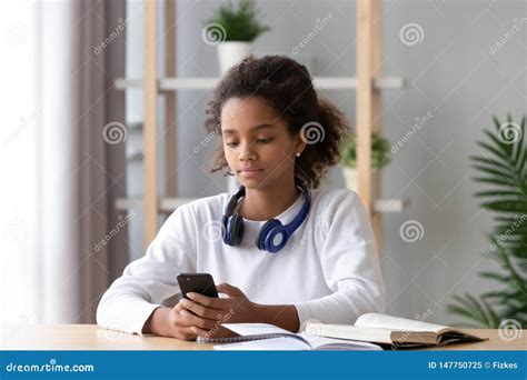 African American Teen Girl Using Phone Distracted From Homework Stock