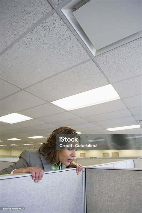 Female Office Worker Peering Over Partition Into Office Cubicle Stock