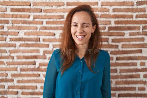 Brunette Woman Standing Over Bricks Wall Winking Looking At The Camera With Expression Cheerful