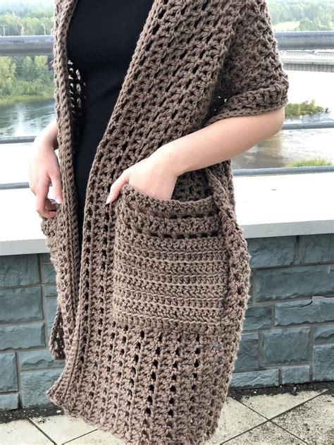 A Woman Wearing A Brown Crochet Cardigan And Black Top With Her Hands