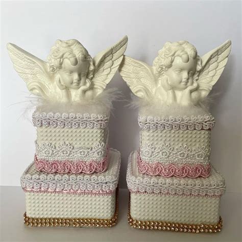 Two White Angel Figurines Sitting On Top Of Boxes With Pink Trimmings