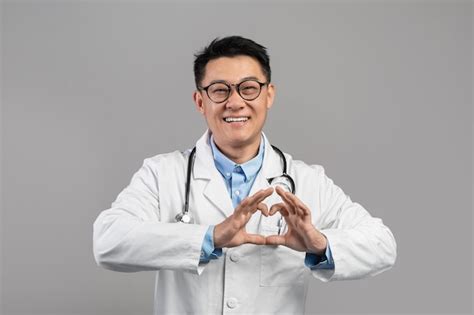 Alegre médico japonés de mediana edad con bata blanca y gafas muestra