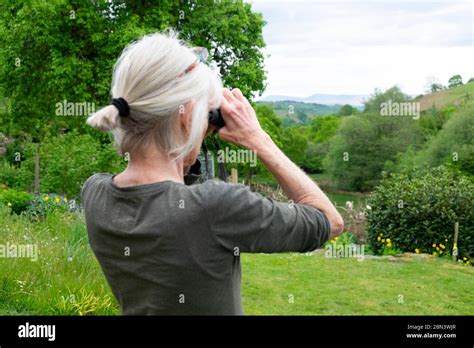 Woman Birdwatching Standing In Country Garden With Binoculars Looking