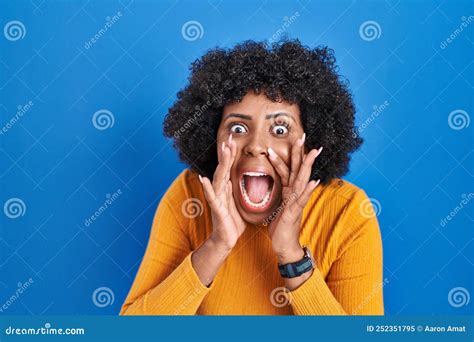 Black Woman With Curly Hair Standing Over Blue Background Shouting Angry Out Loud With Hands