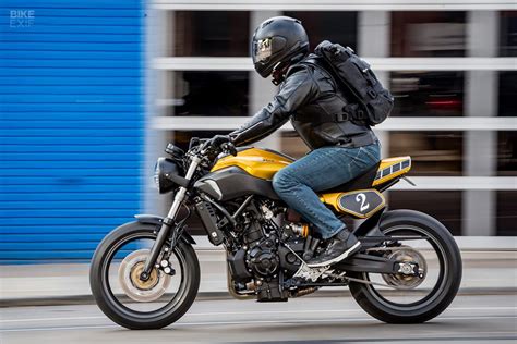 A Man Riding On The Back Of A Yellow Motorcycle Down A Street Next To A