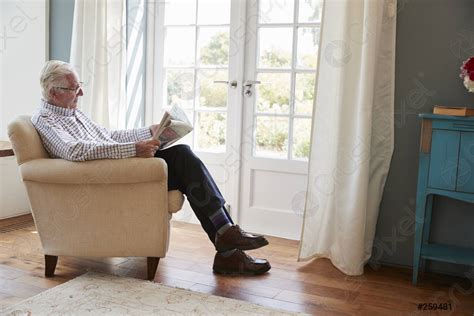 Senior Man Sitting In An Armchair Reading Newspaper At Home Stock