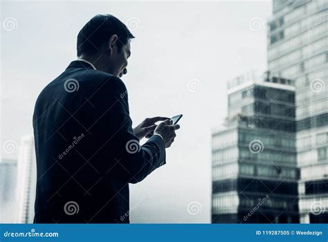 Businessman Using Mobile Phone Near Office Window At Office Building