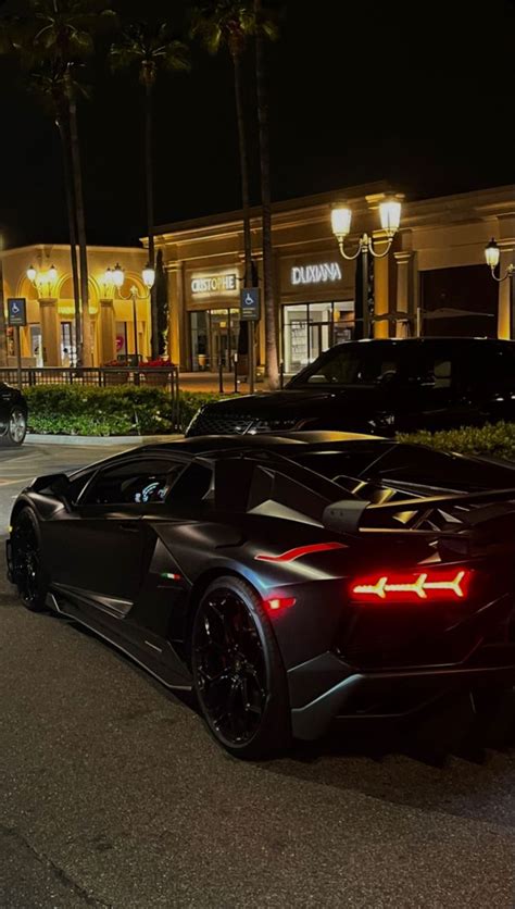 Two Black Sports Cars Parked In Front Of A Building With Palm Trees On