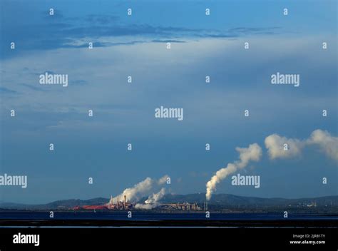 Industrial Landscape With Smokestacks Emitting Smoke Over A Coastal