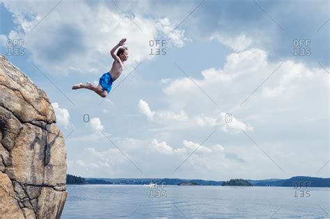 Boy jumping off cliff into sea stock photo - OFFSET