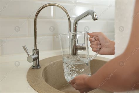 Woman Pouring Water Into Glass Jug In Kitchen Closeup Stock Photo