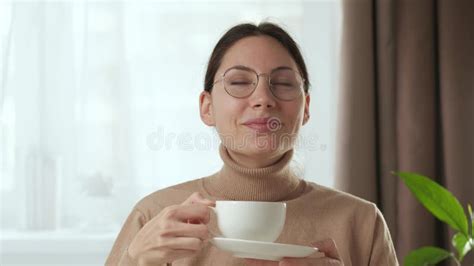 A Pretty Brunette Woman Looks Into The Camera Smiles And Takes A Sip