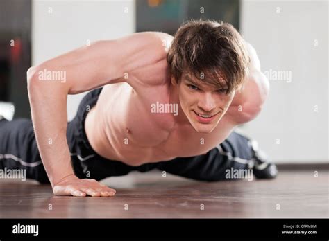 Muscular Man Exercising By Doing Pushups With Only One Arm In A Gym