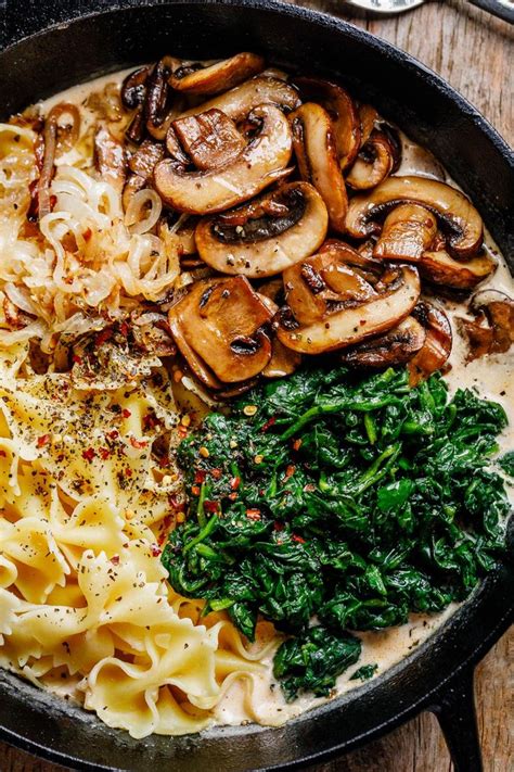 A Pan Filled With Pasta Spinach And Mushrooms On Top Of A Wooden Table