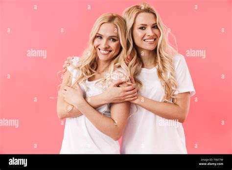 Smiling Blonde Twins Wearing In T Shirts Posing Together And Looking At The Camera Over Pink