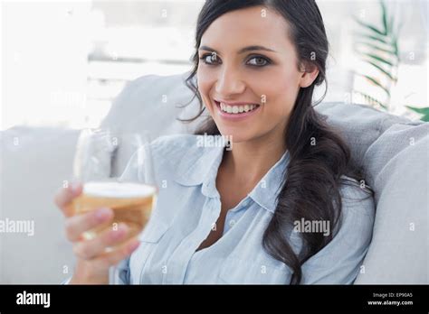 Cheerful Pretty Brunette Drinking White Wine Sitting On Sofa Stock