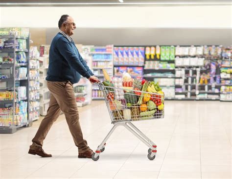 Mature Man In A Supermarket Walking And Pushing A Shopping Cart With