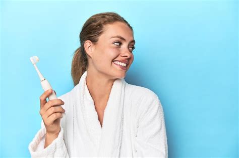 Premium Photo Blonde In Bathrobe With Electric Toothbrush In Studio