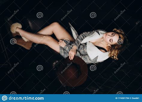 Stylish Blonde In Boots And A Coat On Her Naked Body On A Black Leather Sofa In A Loft Style