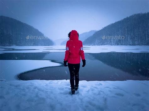 Rear View Of Woman In Red Coat Standing Near A Frozen Lake Stock Photo