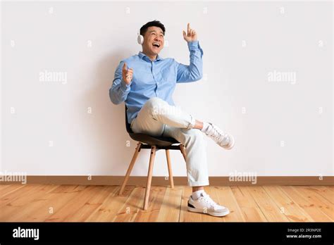 Joyful Asian Mature Man Sitting In Chair Using Headphones Listening To