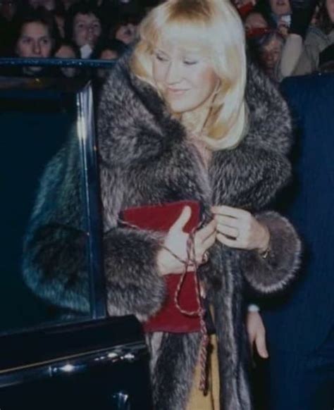 A Woman In A Fur Coat Standing Next To A Car With Other People Behind Her