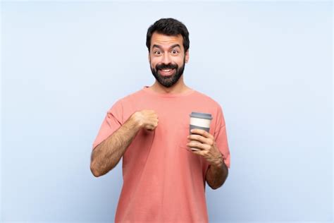 Joven con barba sosteniendo un café para llevar sobre pared azul