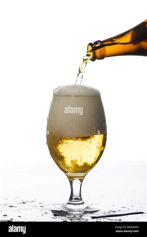 Beer Pouring From Bottle Into Glass On Surface With Puddle Isolated On