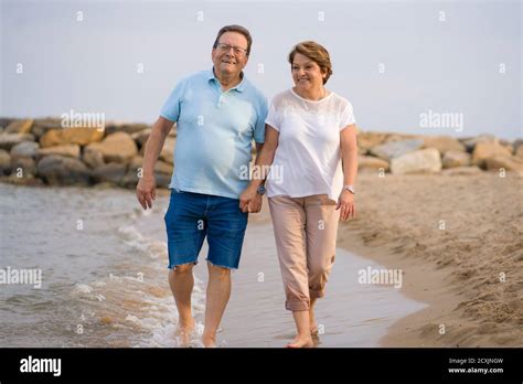 Happy Retired Mature Couple Walking On The Beach Pensioner Woman And Her Husband Taking