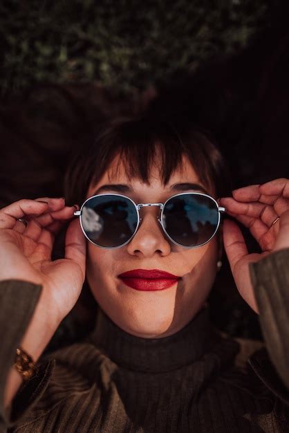 Una mujer joven con gafas de sol tumbada en el césped mostrando su