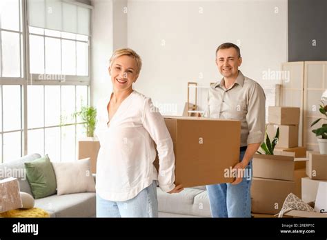 Mature Couple Carrying Cardboard Box In Room On Moving Day Stock Photo